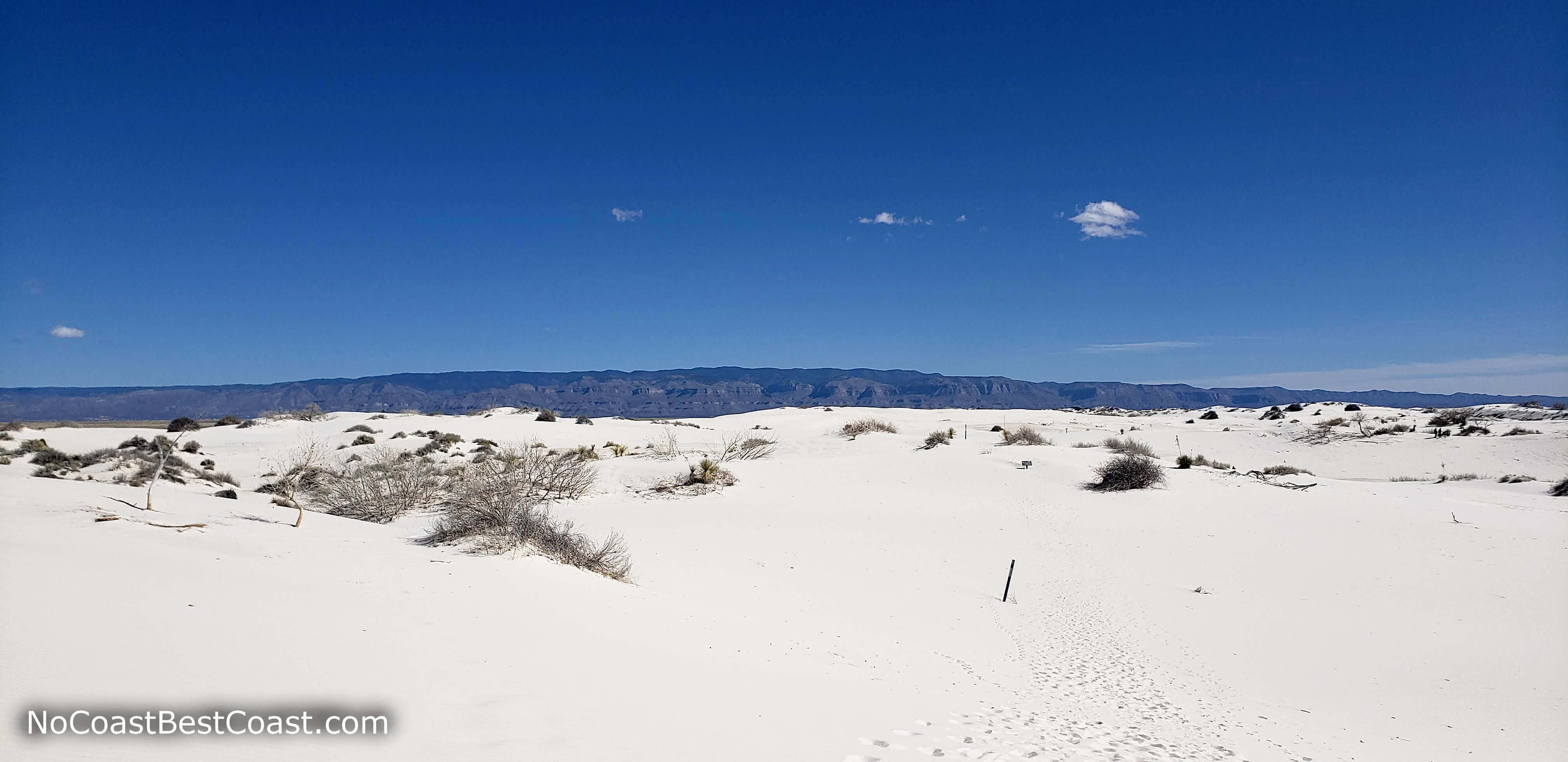 A trail marker in the white sand and the Sacramento Mountains in the distance