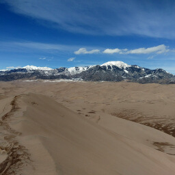 Massive sand dunes with snow capped peaks in the background